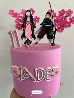 a pink birthday cake with two people on top and flowers in the middle that spell it's 11