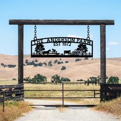 a sign hanging from the side of a wooden gate in front of a lush green field