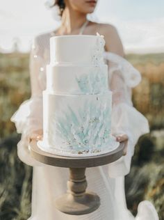 a woman is holding a white wedding cake