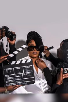 a woman holding a clap board in front of some other people with cameras around her