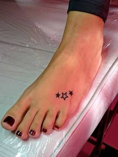 a woman's foot with three stars tattoo on her left toe and black nail polish