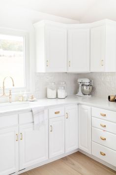 a kitchen with white cabinets and gold handles