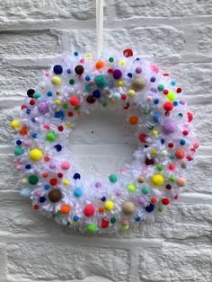 a white wreath with multicolored pom - poms hanging on a brick wall