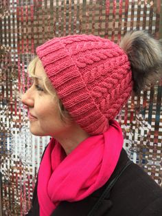 a woman wearing a pink scarf and a knitted hat with pom - poms