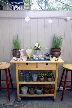 a wooden table topped with potted plants next to two stools