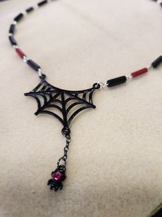 Just in time for Halloween, this spider web necklace is sure to delight. Fully hand made links make this a one-of-a-kind piece. The links feature black and red glass beads. This necklace measures 16.5 inches in total length. The handmade links are crafted from silver filled wire. The closure is a sterling silver lobster claw clasp. It is a very lightweight piece, made from tarnish resistant silver wire, so it is comfortable for all day wear and will last for years to come. And to top it all off, the web is complete with a hanging spider sporting a pink jewel. Black Halloween Necklace With Lobster Clasp, Gothic Black Necklace With Lobster Clasp, Black Gothic Necklace With Lobster Clasp, Adjustable Black Vampire Necklace, Adjustable Black Vampire Style Necklaces, Adjustable Red Necklace For Halloween, Handmade Black Vampire Necklace, Handmade Red Necklaces For Halloween, Handmade Red Halloween Necklaces