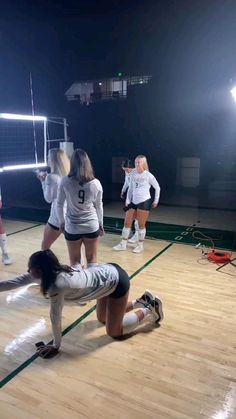 the girls are playing volleyball on the court at night, and one girl is trying to block the ball