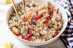 a white bowl filled with pasta salad next to lemon wedges