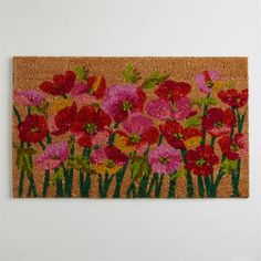 a door mat with red and pink flowers on the front, green grass behind it