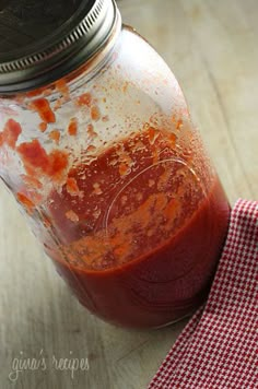 a jar filled with red sauce sitting on top of a wooden table next to a napkin