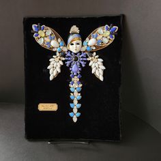 an elaborately decorated brooch sits on a black velvet box with gold and blue accents