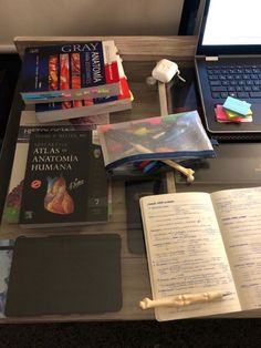 a laptop computer sitting on top of a desk next to a pile of books and other items