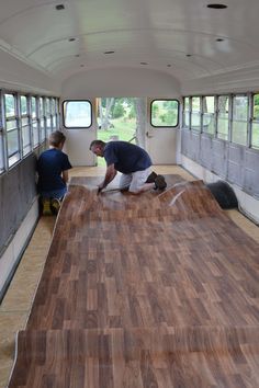 two men are working on the inside of a bus with wood flooring in place