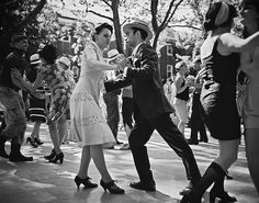 black and white photograph of people dancing on the street with trees in the back ground