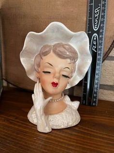 a ceramic figurine of a woman wearing a white hat on a wooden table