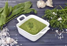 a white bowl filled with green pesto next to garlic and herbs