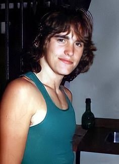 a woman standing in front of a counter with a bottle on it and a sink behind her