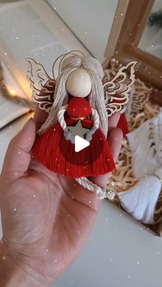 a hand holding a red angel ornament in front of a white christmas tree