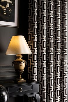 a lamp sitting on top of a table next to a window covered in black and white curtains