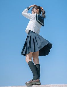 a girl in a skirt and knee high boots is standing on top of a wall