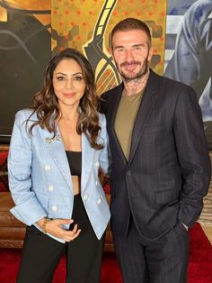 a man and woman standing next to each other on a red carpet in front of a painting