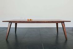 a wooden table sitting on top of a black floor next to a white wall and two glasses