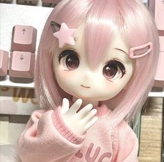 a close up of a doll wearing a pink sweater and holding her hand near her face