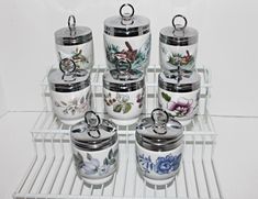 there are many containers on the shelf with lids and spoons in them, all decorated with floral designs