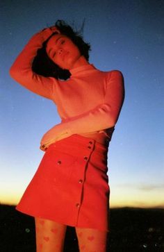 a woman in a red skirt is posing for the camera with her hands on her head