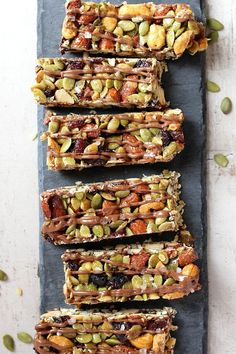 five pieces of granola bars on a slate board with nuts and seeds scattered around them