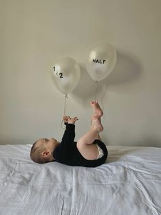 a baby laying on top of a bed holding balloons