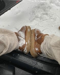 someone is holding their feet in the snow while wearing brown boots and socks on top of a car