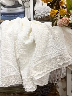 white linens are stacked on top of each other in front of some vases with flowers