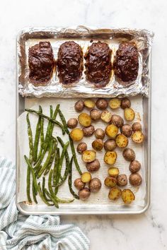 roasting potatoes and green beans on a baking sheet with tinfoil over them, ready to be cooked