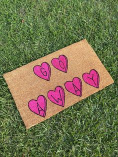 a door mat with pink hearts drawn on it in the middle of some green grass