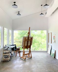 an artist's easel is in the middle of a room with large windows