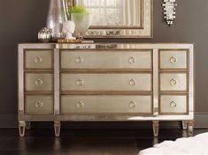 an ornate dresser with mirror and vase on top in front of it, next to a white sheepskin rug