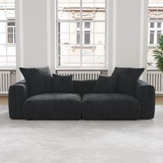 a black couch sitting in an empty room next to two windows and a potted plant