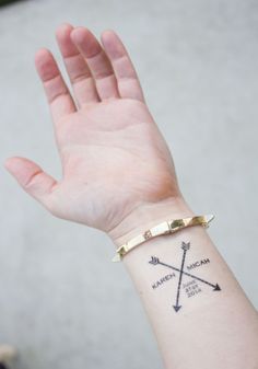 a woman's arm with an arrow tattoo on her left wrist and gold bracelet