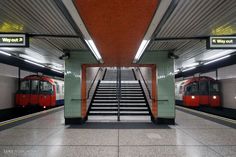 two trains parked in a subway station next to each other with stairs leading up to them