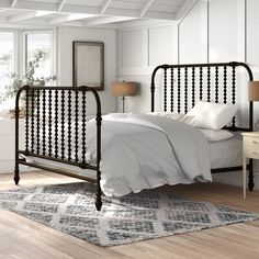 a bedroom with white walls and wood flooring has a black iron bed frame on top of a rug