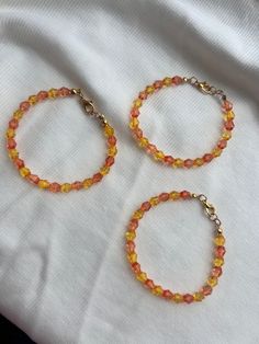 two orange and yellow beaded bracelets sitting on top of a white cloth covered bed