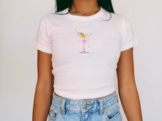 Martini Baby Tee   Women's T-Shirt | Girly Aesthetic | Y2K Trendy Shirt 🌟SHIRT This is a Bella+Canvas baby tee - the material is very soft and very high quality. 🌟SIZING Please find the size chart in listing photo before purchasing. We recommended measuring a t-shirt you already own to get the best fitting t-shirt. 💖CARE/ WASH Machine wash: warm (max 40C or 105F); Non-chlorine: bleach as needed Tumble dry: medium heat; Iron, steam or dry: low heat; Do not dry clean. ✨SHIPPING Your items usually will ship in 2-7 business days. Products shipped from US.  Thanks for shopping small.  Please let me know if you need any custom designs or bulk orders that is not listed, I'll happily custom-make it for you! ♡ Cute Fitted Summer T-shirt, Cute Fitted White T-shirt, Cute Fitted Shirt With Graphic Print, Cute Fitted Cotton Shirt, Pink Fitted Graphic Tee, Fitted Cute Shirt With Graphic Print, Fitted Shirt With Graphic Print In Cute Style, Fitted Pink Graphic Tee Shirt, Cute Fitted Pink T-shirt