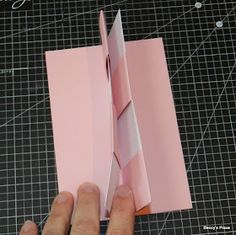 someone is making a paper airplane out of pink paper on a cutting mat with scissors