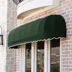 a green awning on the side of a brick building with white trim and windows