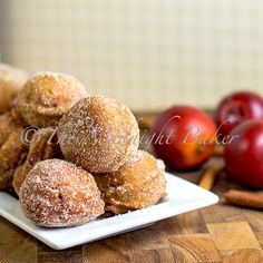 some sugared donuts on a white plate with cinnamon sticks and apples in the background