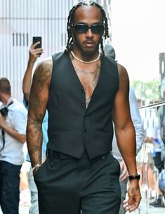 a man with dreadlocks walking down the street in a black suit and sunglasses