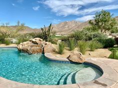 an outdoor pool with rocks and water features a waterfall, palm trees, and mountains in the background