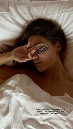 a woman laying in bed with her eyes closed and eyeliners painted on her face