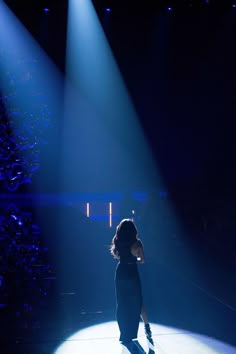 a woman standing in the middle of a stage with lights on her head and hands behind her back